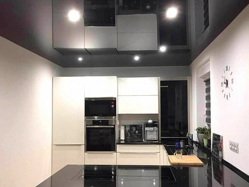Moderne schwarz-weiße Küche mit schwarzer Hochglanz-Spanndecke, integrierten LED-Einbaustrahlern und glänzenden Oberflächen